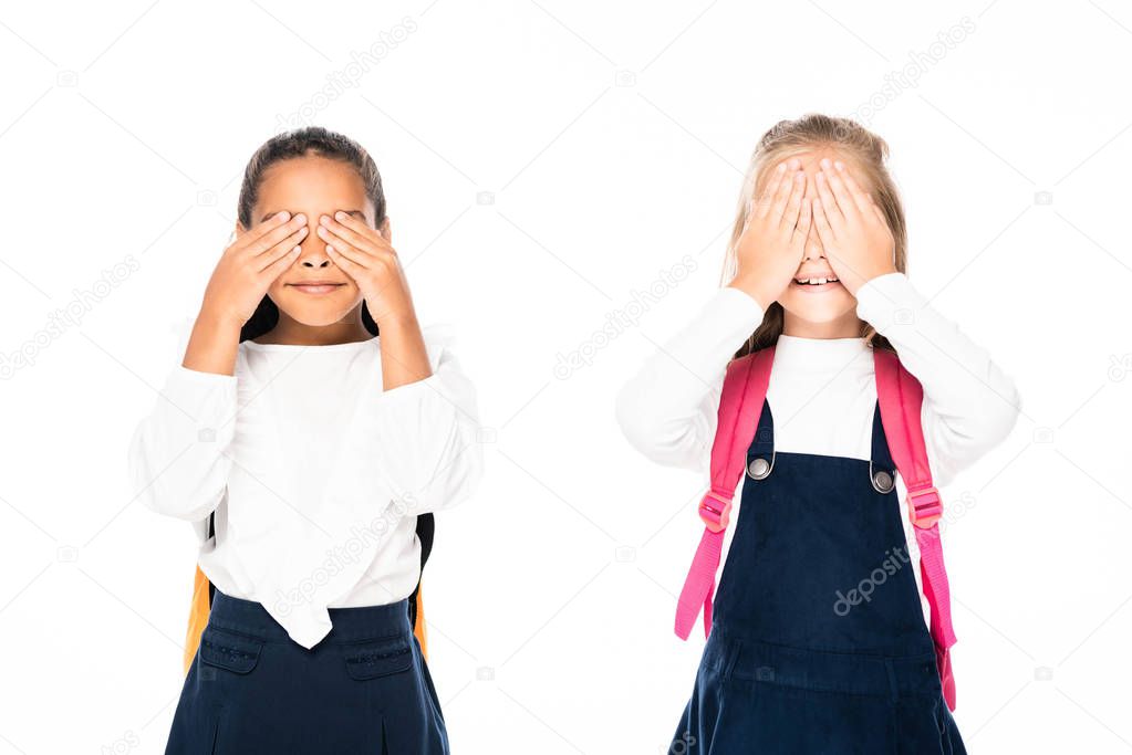 two multicultural schoolgirls covering faces with hands isolated on white