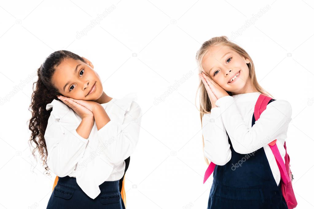 two smiling, tired multicultural schoolgirls looking at camera isolated on white