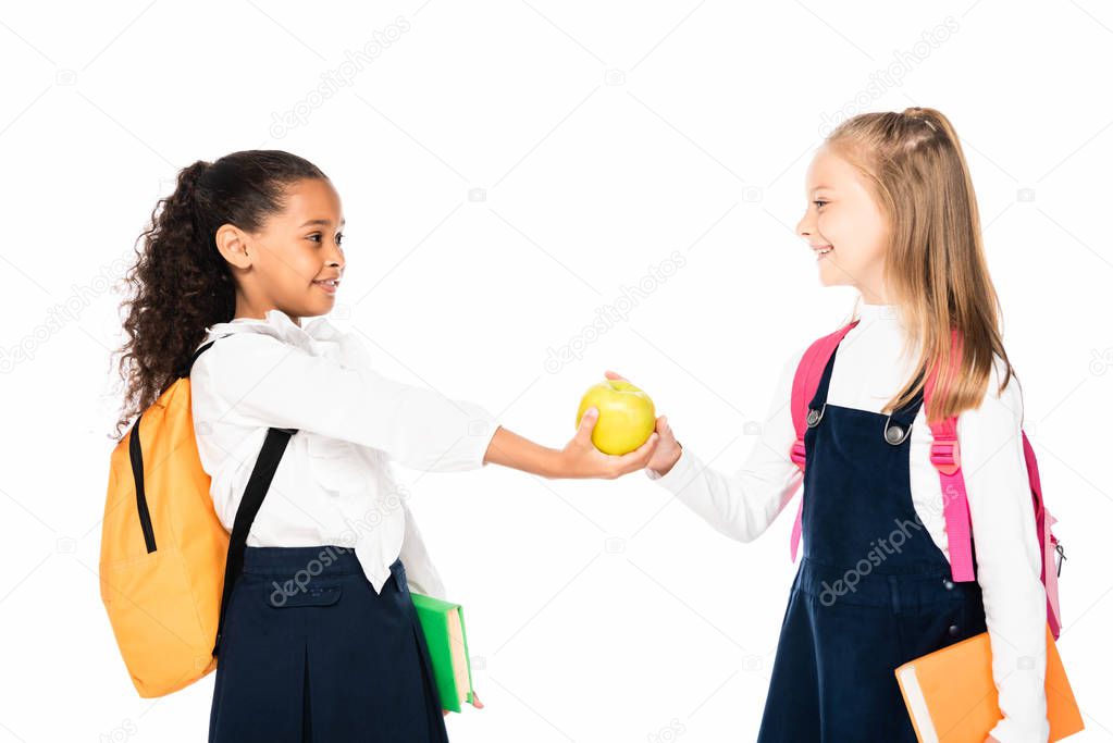 cheerful african american schoolgirl giving apple to friend isolated on white