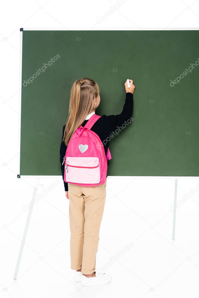 back view of schoolgirl with pink backpack writing on green chalkboard on white background