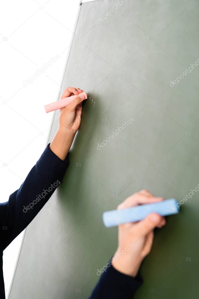cropped view of two multicultural schoolgirls writing on chalkboard isolated on white