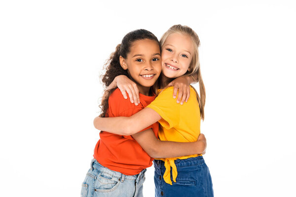 two happy multicultural friends embracing while looking at camera isolated on white