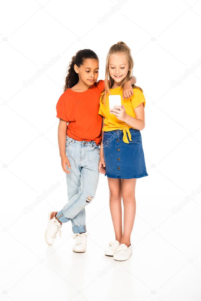 full length view of cute african american kid hugging friend using smartphone on white background