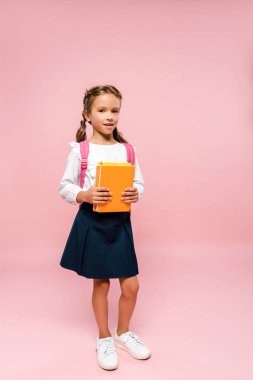 pembe sırt çantası ile ayakta iken kitap tutan mutlu çocuk 