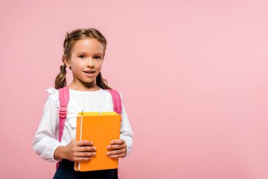 pembe izole sırt çantası ile ayakta iken kitap tutan mutlu çocuk 
