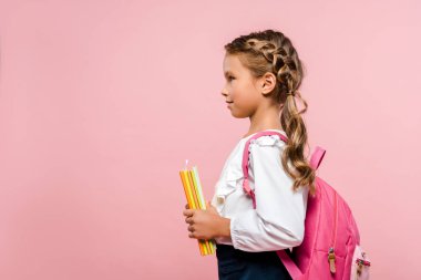 pembe izole sırt çantası ile ayakta iken kitap tutan mutlu çocuk yan görünümü 