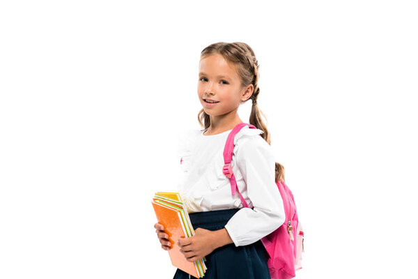 cheerful child holding books and standing with backpack isolated on white 