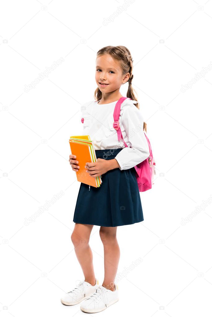 cheerful child holding books and standing with pink backpack isolated on white 