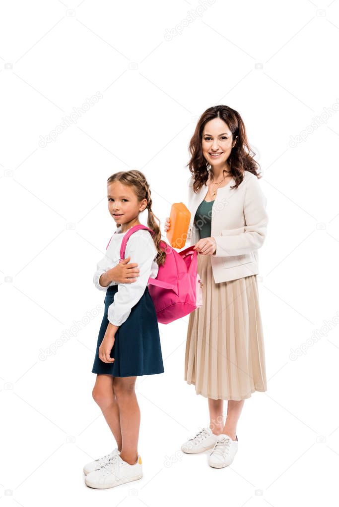 happy mother putting book in backpack of cute daughter isolated on white