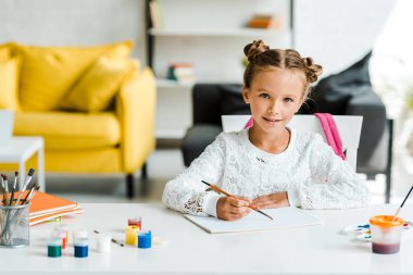 mutlu çocuk masaüzerinde guaj kavanoz ve kağıt yakınında paintbrush tutan 
