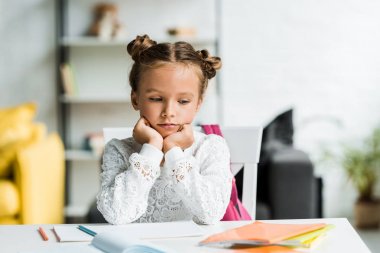 üzgün çocuk oturma ve masadaki kitaplara bakarak 