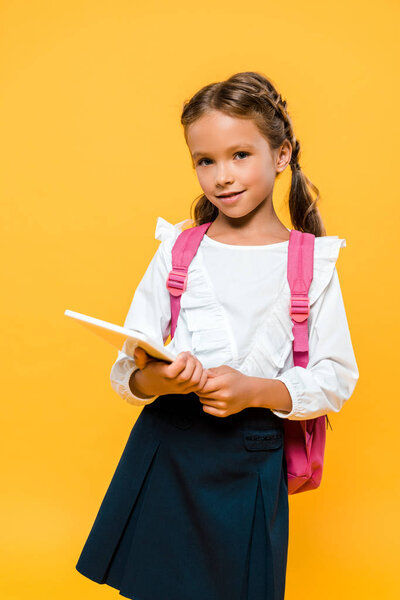 happy schoolchild with pink backpack holding book isolated on orange 