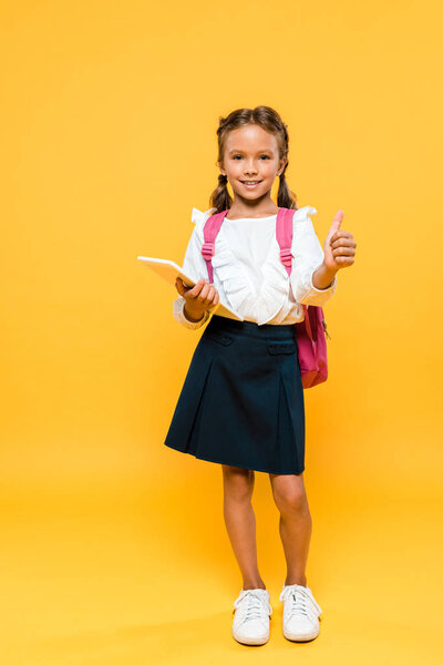 happy schoolkid holding books and showing thumb up on orange 