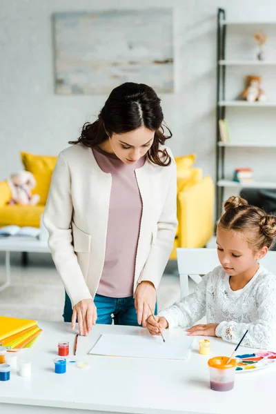 Attraktive Mutter Steht Neben Tochter Und Hält Pinsel Neben Papier — Stockfoto