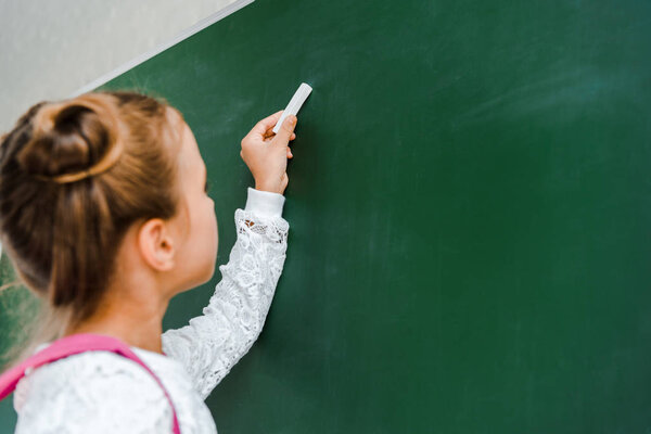 selective focus of schoolgirl holding chalk near green chalkboard 