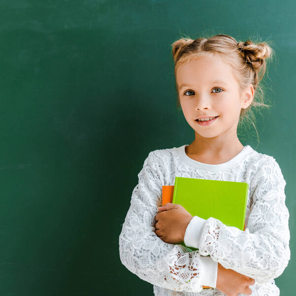 happy schoolgirl smiling while standing with books on green 