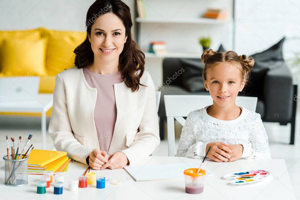 happy young woman sitting with cute daughter near gouache jars 