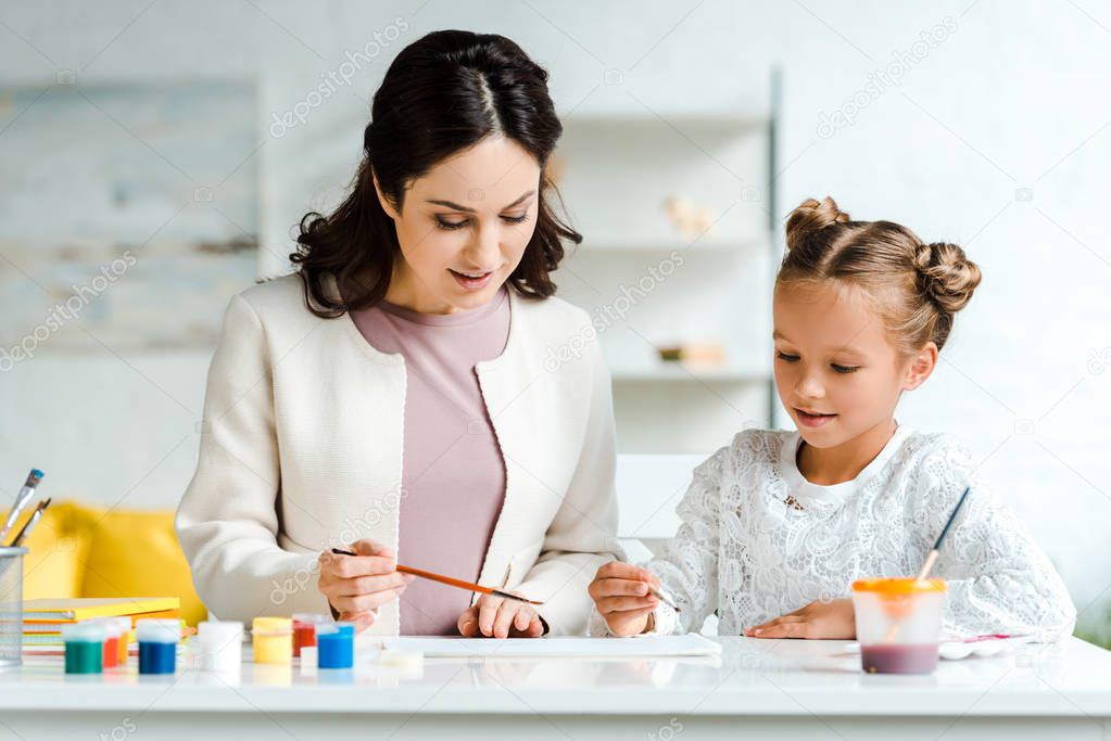 happy young woman painting with cute daughter at home 