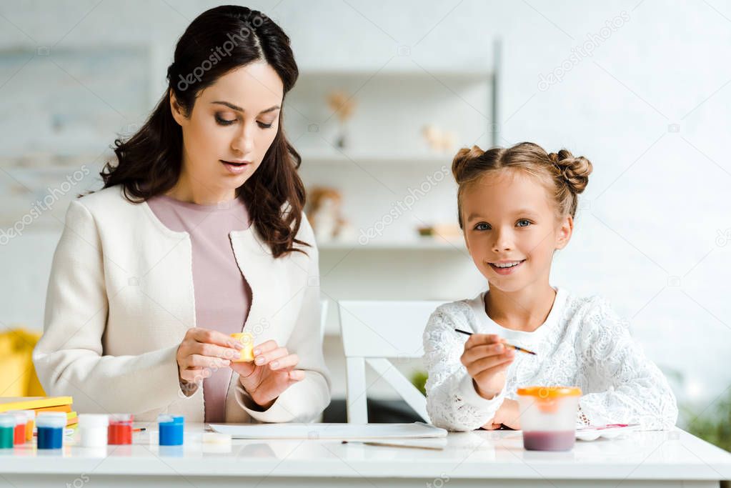 attractive mother holding gouache jar near happy daughter 