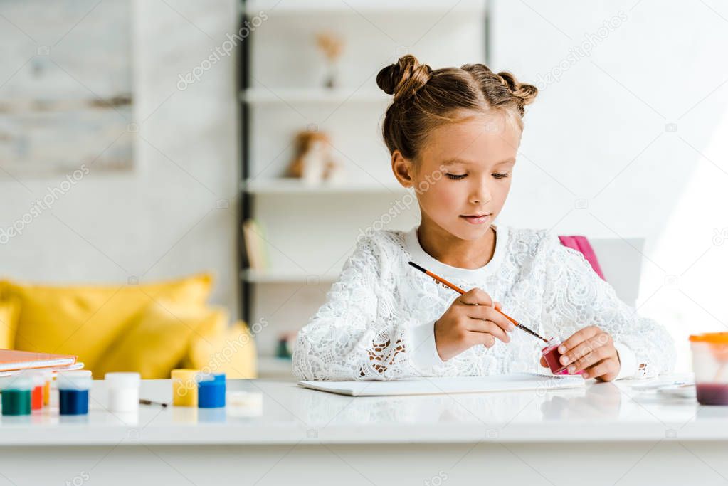 cute kid holding paintbrush near gouache jars on table 