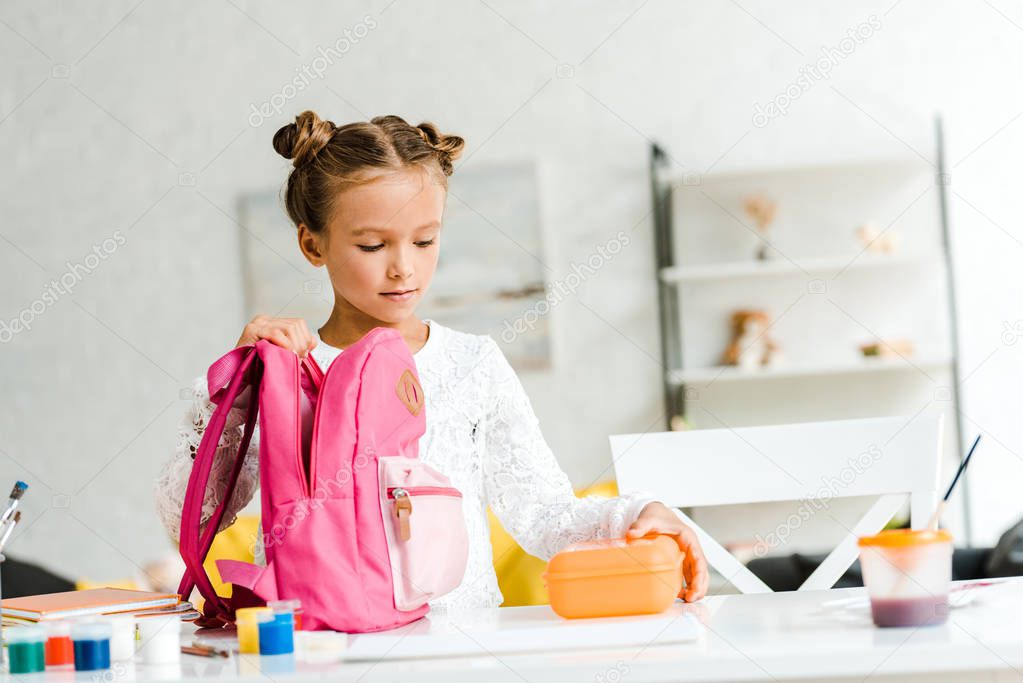 cute schoolgirl holding lunch box near pink backpack 