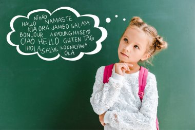 pensive kid standing with backpack near chalkboard with greetings lettering on green  clipart