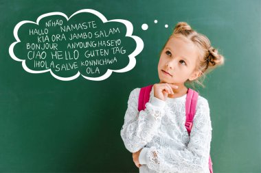 pensive kid standing with backpack near chalkboard with greetings lettering on green  clipart