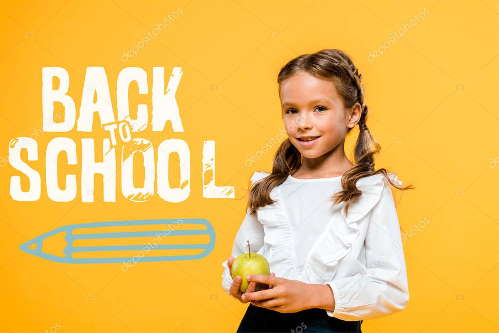 happy schoolchild holding tasty apple near back to school lettering on orange 