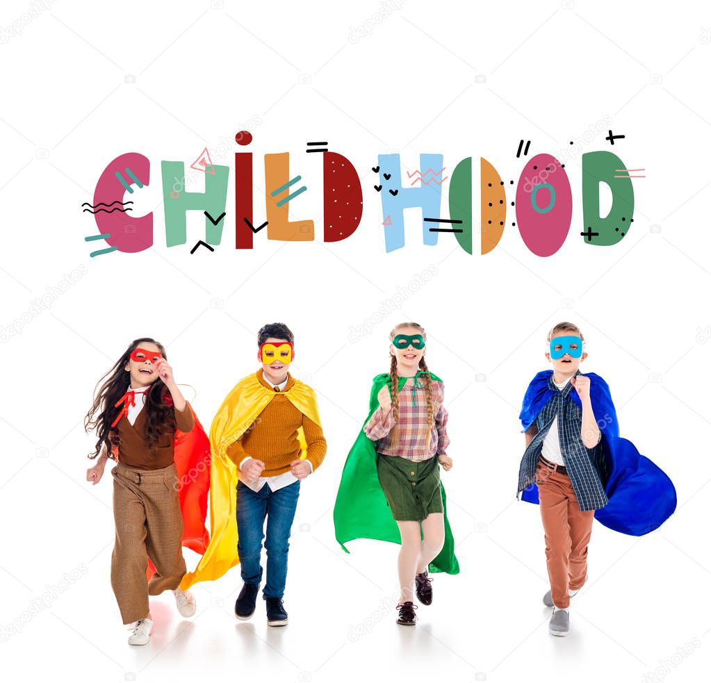 happy kids in superhero costumes and masks running near childhood lettering on White