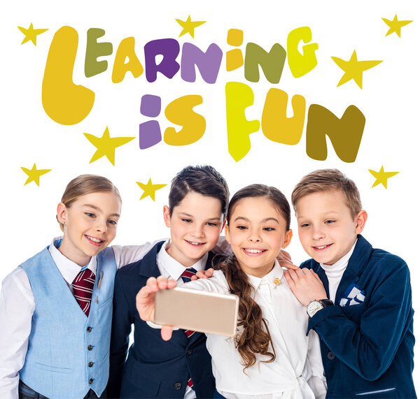 happy schoolchildren taking selfie on smartphone near learning is fun letters on white
