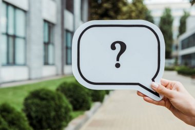 cropped view of woman holding speech bubble with question mark near building  clipart