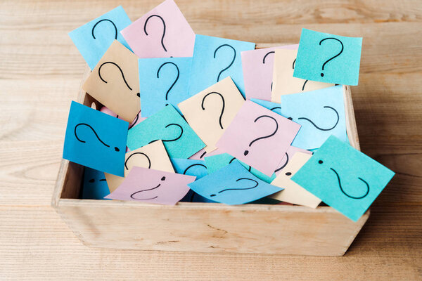 overhead view of sticky notes with question marks in wooden box on desk 