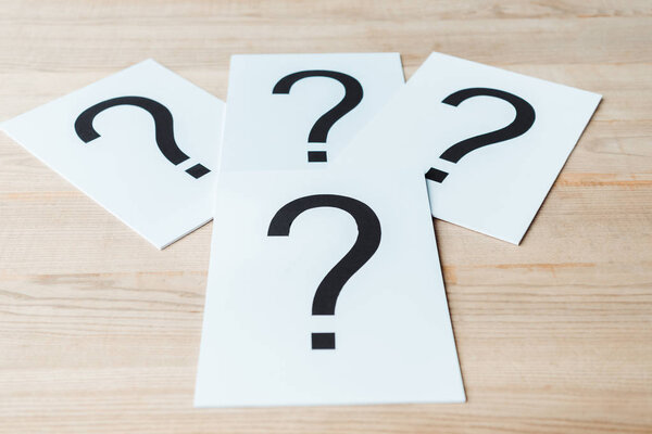 black question marks on white papers on wooden desk 