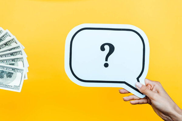 cropped view of woman holding speech bubble with question mark near dollar banknotes on orange 