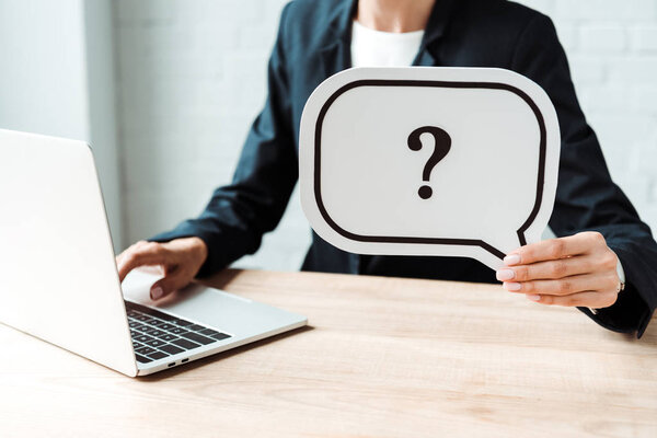 cropped view of woman holding speech bubble with question mark while working in office 