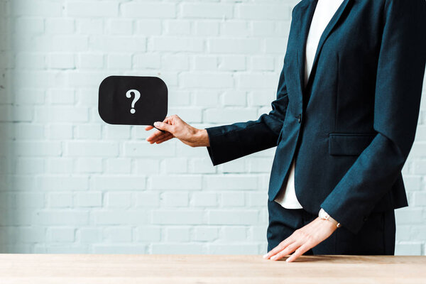cropped view of woman holding black speech bubble with question mark while standing in office 