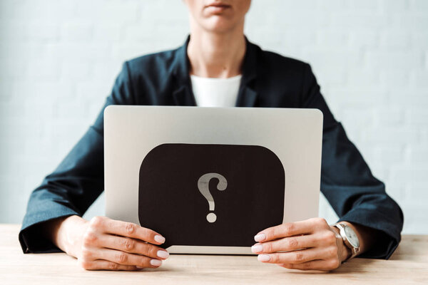cropped view of woman holding black speech bubble with question mark while sitting in office 