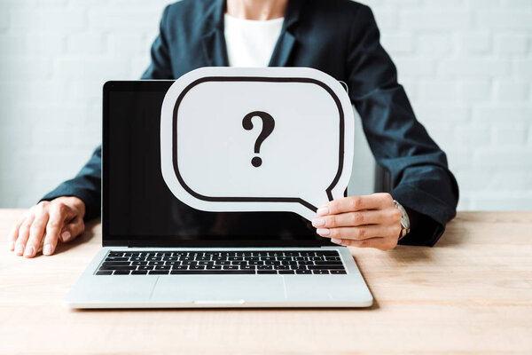 cropped view of woman holding speech bubble with question mark near laptop