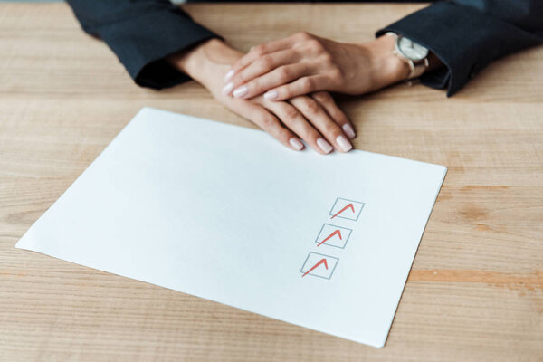 cropped view of businesswoman with clenched hands near check list 