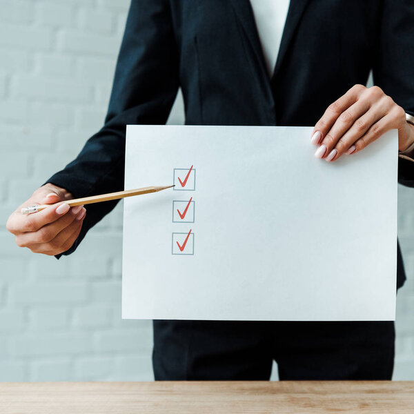 cropped view of businesswoman holding pencil near paper with check list 