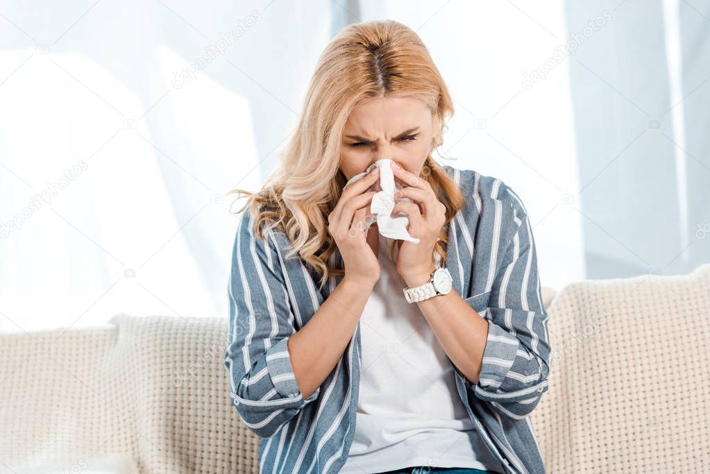 sick woman sitting on sofa and sneezing in napkin 