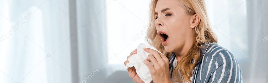 panoramic shot of woman holding napkin and sneezing at home 