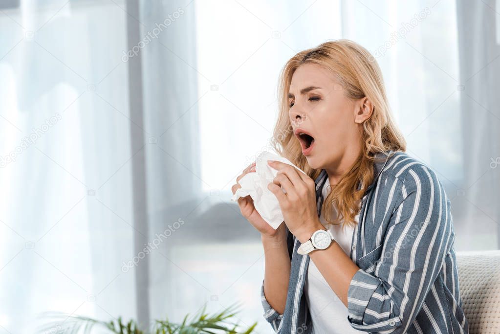 woman with closed eyes holding napkin and sneezing at home 