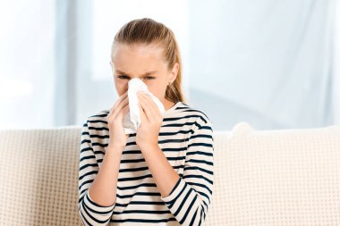 diseased kid sneezing in tissue and looking at camera  clipart