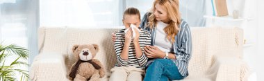 panoramic shot of woman sitting near daughter sneezing in tissue near teddy bear  clipart