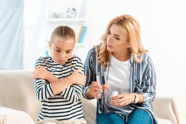 çocuk yakınında haplar ile su ve şişe ile cam tutan anne 