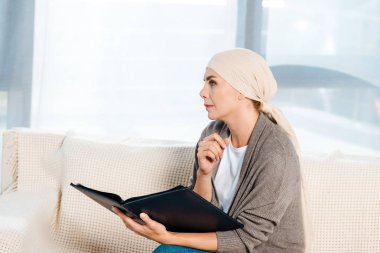 oturma odasında fotoğraf albümü tutan başörtüsü ile hasta kadın 