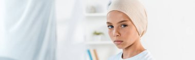 panoramic shot of sick kid in head scarf looking at camera clipart