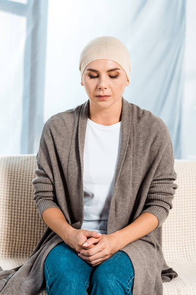 sick woman in head scarf sitting on sofa 