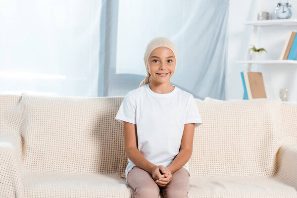 happy kid in head scarf sitting on sofa in living room 